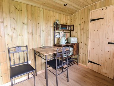 A wooden kitchen area with a table two chairs kettle toaster and shelves at The Oak Hut in Coton near Whitchurch