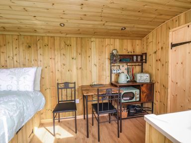 A small wooden room with a bed a table two chairs and a kitchenette with appliances and kitchenware at The Oak Hut in Coton near Whitchurch