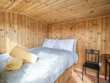 A bedroom with a bed with pillows and rolled towels a black chair and wooden walls and ceiling at The Oak Hut in Coton near Whitchurch