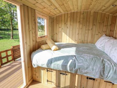 A wooden interior bedroom with a bed and window overlooking a green field at The Oak Hut in Coton near Whitchurch