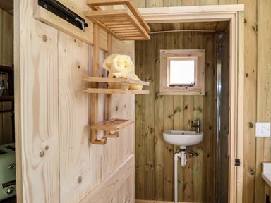 A small bathroom with wooden walls a small sink a window and wooden shelves with towels at The Oak Hut in Coton near Whitchurch