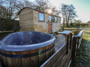 An outdoor wooden hut with two windows and a door next to a large round hot tub on a wooden deck at The Oak Hut in Coton near Whitchurch