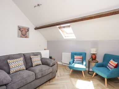 A living room with a grey sofa two blue armchairs a skylight window and a side table with a lamp at Stabal Bach in Criccieth