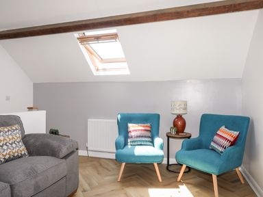 A sitting area with two blue chairs and a side table with a lamp and plants under a skylight at Stabal Bach in Criccieth