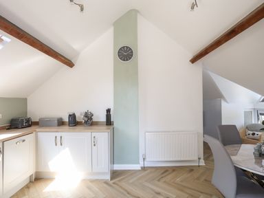 A kitchen corner with white cabinets wooden countertop appliances and a wall clock next to a dining area at Stabal Bach in Criccieth