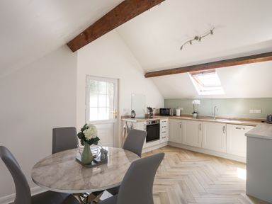 A kitchen with a round dining table and chairs under exposed beams at Stabal Bach in Criccieth