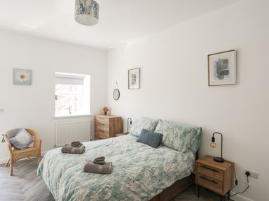 A bedroom with a double bed two nightstands wall art a wicker chair and a chest of drawers at Stabal Bach in Criccieth
