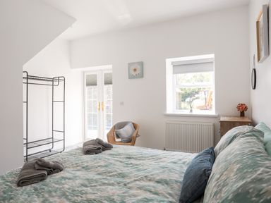 A bedroom with a bed folded towels a clothes rack a wicker chair and a window at Stabal Bach in Criccieth