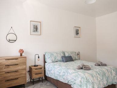 A bedroom with a bed with patterned bedding two bedside tables with lamps a chest of drawers with flowers a round mirror and two framed pictures on the wall at Stabal Bach in Criccieth