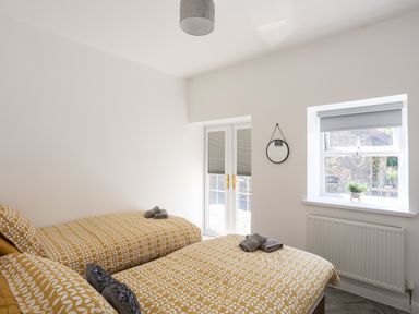 A bedroom with two single beds yellow patterned bedding a small round mirror window and glass doors at Stabal Bach in Criccieth