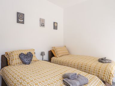 A bedroom with two single beds with yellow patterned bedding and folded grey towels on them at Stabal Bach in Criccieth