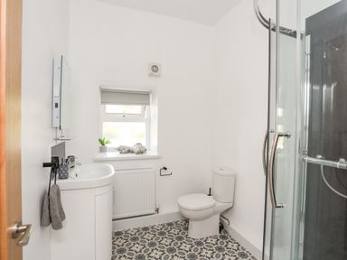 A bathroom with a sink cabinet toilet patterned floor tiles and a curved glass shower enclosure at Stabal Bach in Criccieth