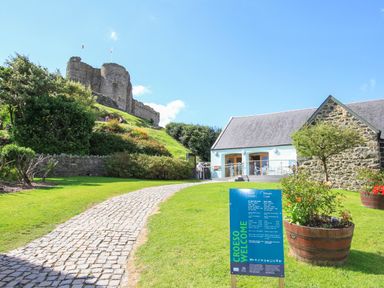 A cobblestone path leading to a castle on a hill with a stone building and a welcome sign on the grass at Stabal Bach in Criccieth