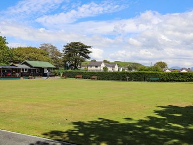 An open lawn with benches and a small building with a person near it at Stabal Bach in Criccieth