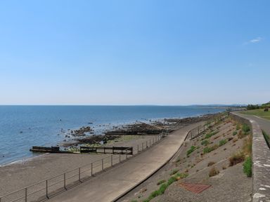 A coastal walkway with railings next to a rocky shore and the sea at Stabal Bach in Criccieth