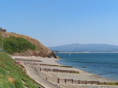 A coastal walkway beside a beach with wooden barriers and hills in the background at Stabal Bach in Criccieth