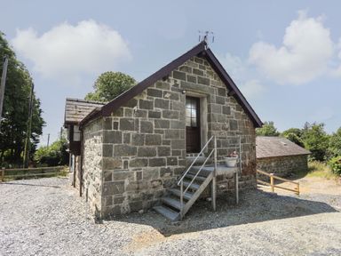 Stone building with metal stairs leading to a door and potted plant outside at Stabal Bach in Criccieth