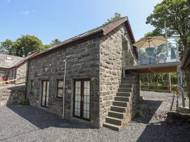A stone building with outdoor stairs leading to a balcony with a table umbrella and chairs at Stabal Bach in Criccieth
