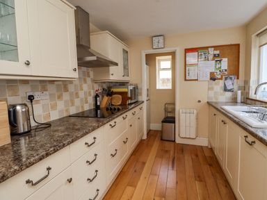 A kitchen with cream cabinets and brown countertops a stove a kettle a microwave a sink and a bulletin board at Victoria House in Alnwick