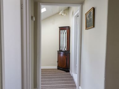 A hallway with a corner cabinet striped carpet and a small painting on the wall at Victoria House in Alnwick