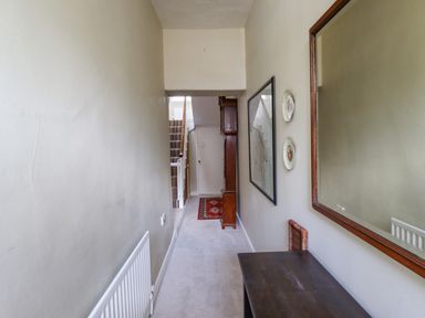 A hallway with a staircase carpet a wooden cabinet a red rug a wall mirror decorative plates and a wooden table at Victoria House in Alnwick