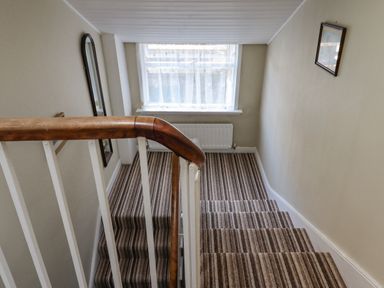 A stairwell with brown striped carpet a wooden handrail a window with sheer curtains a radiator and a wall mirror at Victoria House in Alnwick
