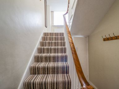 A staircase with striped carpet and wooden handrail with hooks on the wall at Victoria House in Alnwick