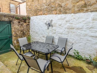 An outdoor patio with a glass table and six chairs against a stone wall with a butterfly decoration