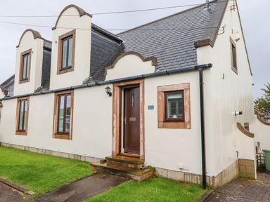 Exterior view of a cream colored cottage with multiple windows and a brown door at Cullernose Cottage Newton-by-the-Sea near Embleton