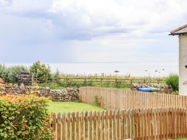 A backyard with wooden and stone fences overlooking a sea with boats at Cullernose Cottage Newton-by-the-Sea near Embleton