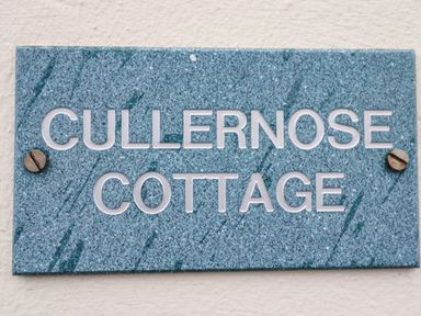 A blue speckled nameplate with white letters reading Cullernose Cottage mounted on a white wall at Cullernose Cottage in Newton-by-the-Sea near Embleton