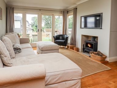A living room with a beige sofa an ottoman a black armchair a fireplace and a wall-mounted TV at Cullernose Cottage Newton-by-the-Sea near Embleton