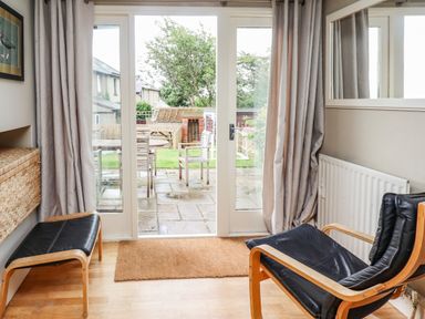 A room with wooden floor cushions and a black chair facing glass doors opening to a garden at Cullernose Cottage in Newton-by-the-Sea near Embleton