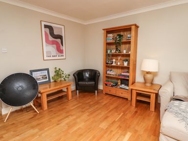 A living room with wooden furniture including a bookcase a coffee table and a side table a black chair a lamp a photo frame plants and a beige sofa at Cullernose Cottage Newton-by-the-Sea near Embleton