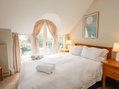 A bedroom with a double bed white linens bedside tables with lamps and an arched window with curtains at Cullernose Cottage in Newton-by-the-Sea near Embleton