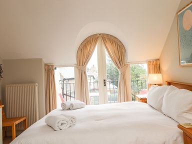 A bedroom with a bed with white linens and rolled towels next to a window with beige curtains and a bedside table with a lamp at Cullernose Cottage Newton-by-the-Sea near Embleton