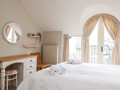 A bedroom with a bed with rolled towels on it a desk with a stool and a chair near a window with curtains at Cullernose Cottage in Newton-by-the-Sea near Embleton