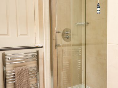 A bathroom with a glass shower enclosure and a chrome towel rack holding a brown towel at Cullernose Cottage Newton-by-the-Sea near Embleton