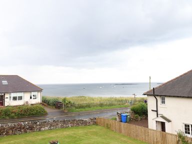 A coastal view with houses a road grassy area and boats on the sea at Cullernose Cottage Newton-by-the-Sea near Embleton