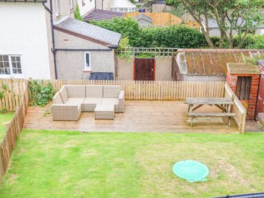 A fenced backyard with a wooden deck patio table and outdoor sofa at Cullernose Cottage Newton-by-the-Sea near Embleton
