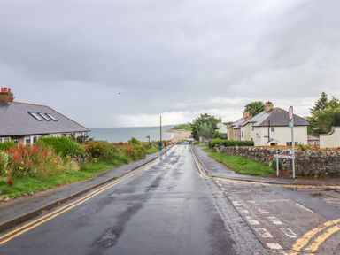 A wet paved road leading to a beach with houses and grass on either side at Cullernose Cottage Newton-by-the-Sea near Embleton