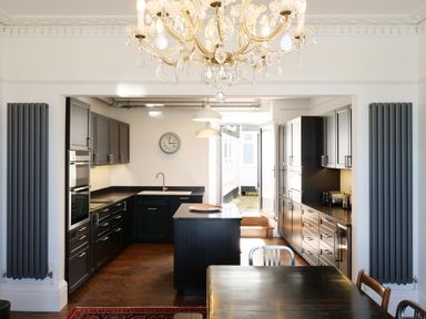 A kitchen with black cabinets a chandelier and dining table at Waves End in St Ives