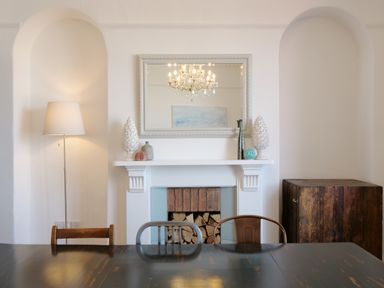 A dining room with a dark table and chairs a white fireplace with decorative items and a large mirror above at Waves End in St Ives