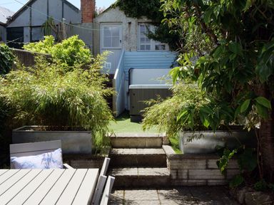 An outdoor patio with a table and chairs surrounded by plants and a raised area with stairs and a door at Waves End in St Ives