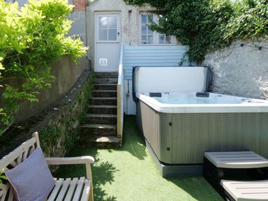 An outdoor area with a hot tub bench with a cushion stairs and a white door at Waves End in St Ives