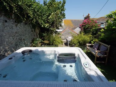 An outdoor hot tub with water surrounded by plants a wooden bench with cushions and a dining table at Waves End in St Ives