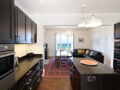 A kitchen with black cabinets and a dining area with a wooden table and sofa at Waves End in St Ives