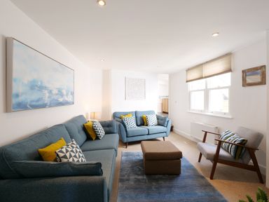 A living room with two blue sofas, an armchair, a brown ottoman, and a blue rug at Waves End in St Ives