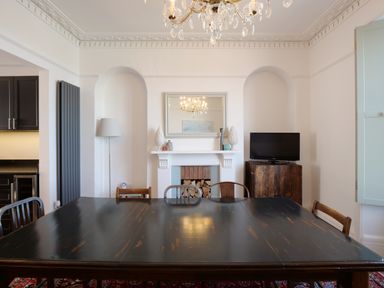 A dining room with a large wooden table chairs fireplace a mirror and a television at Waves End in St Ives