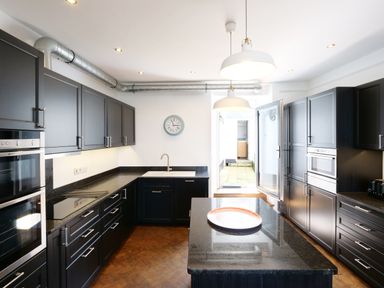 A kitchen with dark cabinets a central island and a clock on the wall at Waves End in St Ives